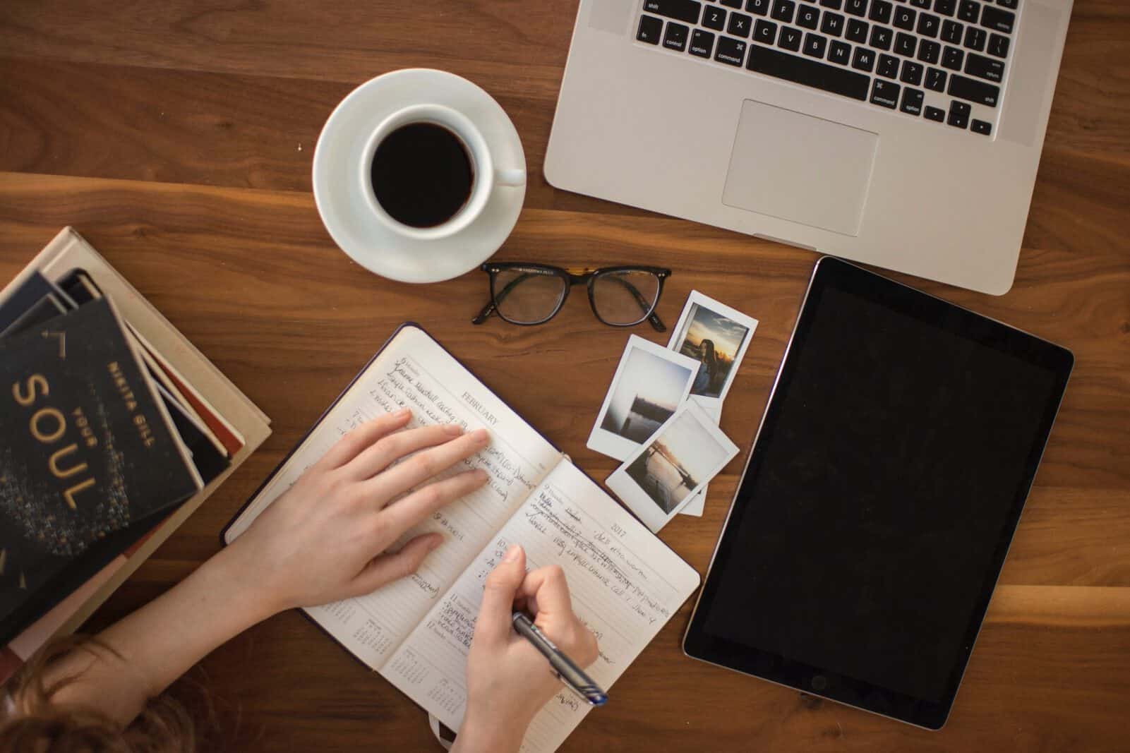 A person at a desk writing in a notebook with a laptop and coffee on the desk showing how to apply to the Australia working holiday visa.