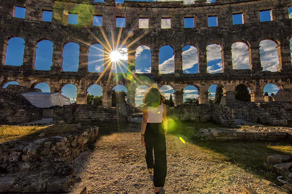 Nina walking among historic Croatian ruins under the sunlight.