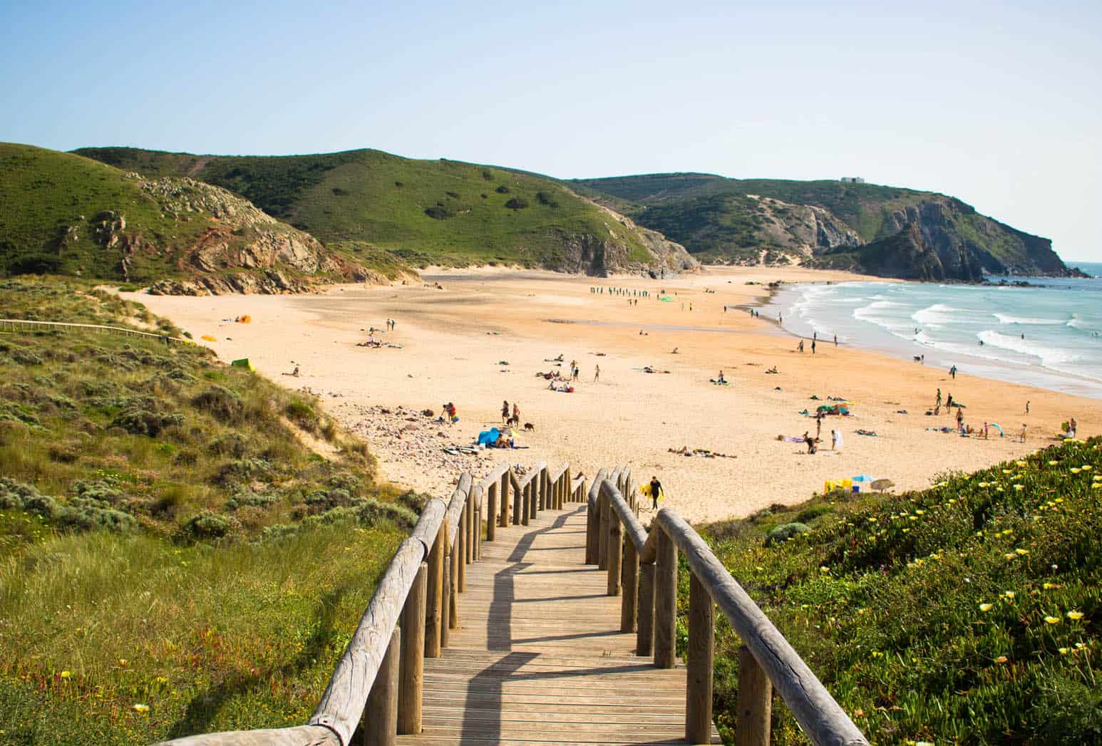 Stairs leading down to Amado Beach in Portugal, where tourist bask in the golden hour light.
