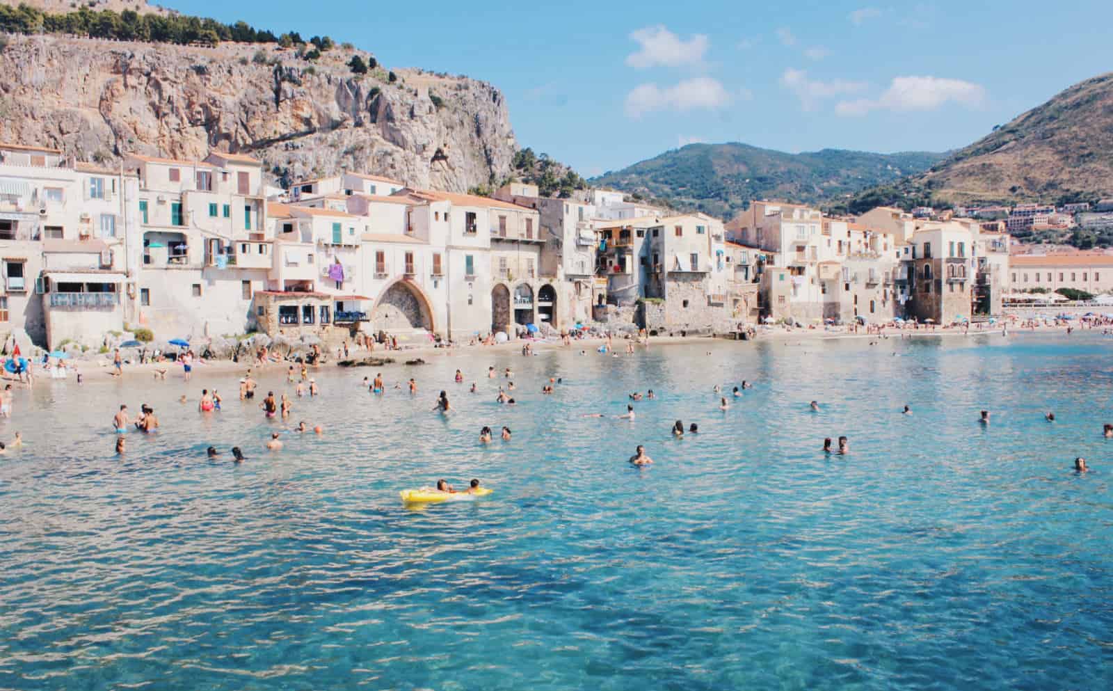 Tourists swimming in the crystal blue ocean waters of eastern Sicily.