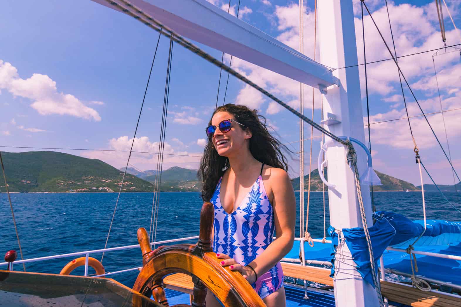 Nina standing at the helm of a sail boat and smiling.
