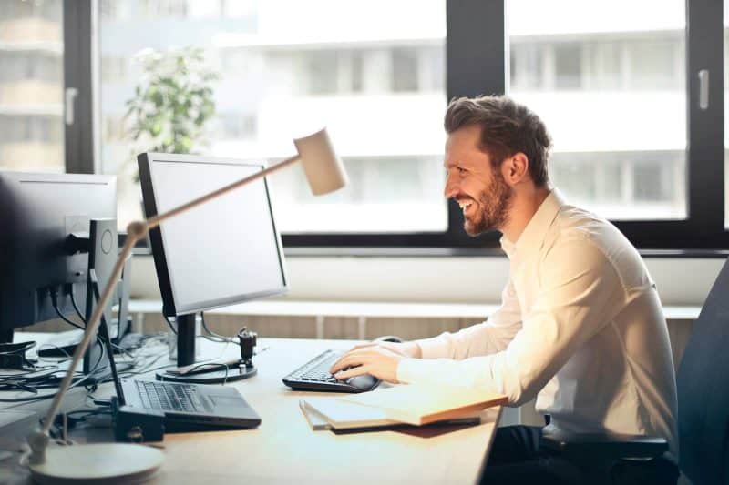 man in office behind at desk smiling teaching English online without a degree