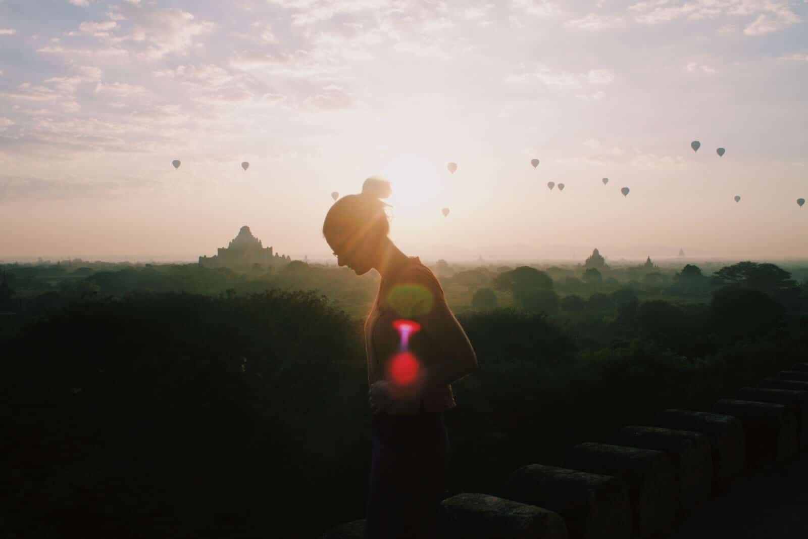 Bagan at sunrise with a woman and hot air balloons silhouette.