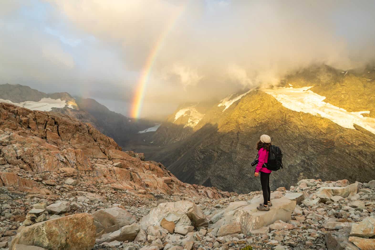 Woman on hike with rainbow in the back representing pros and cons of living abroad.
