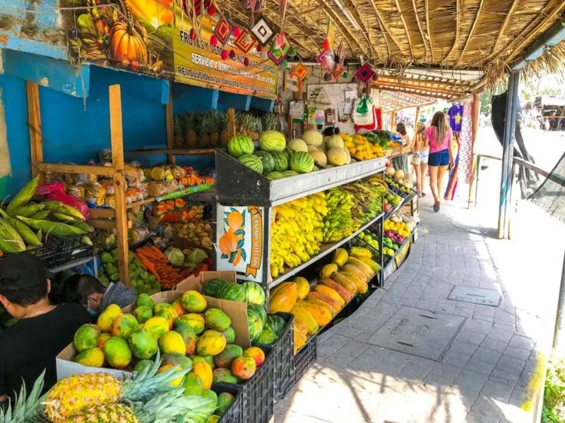 Fruit and vegetable shop on the side of the sidewalk with woman walking past in Sayulita