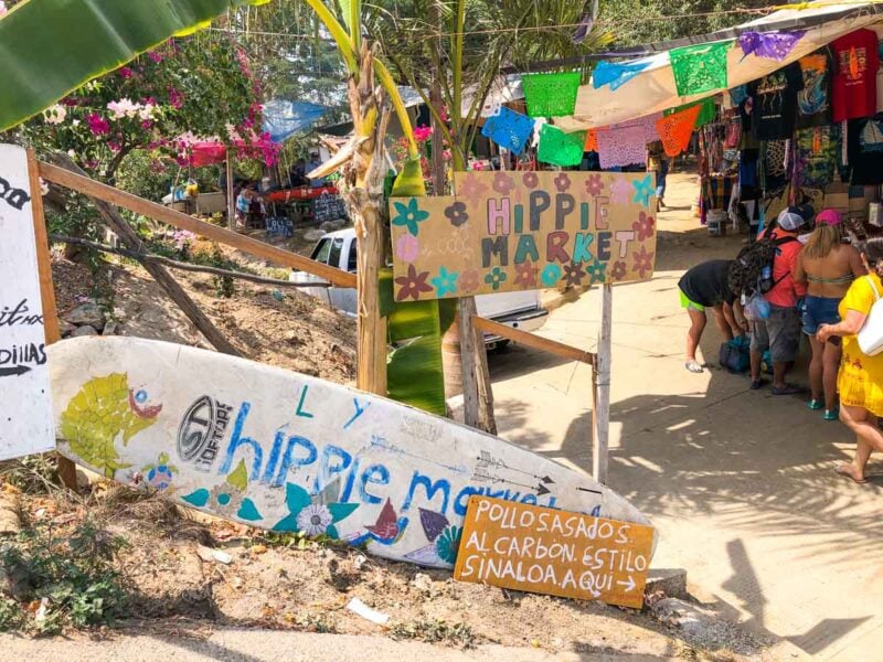 Signs stating Hippie Market in the sand with colorful prayer flags hanging in trees - visiting the market is one of the best things to do in Sayulita