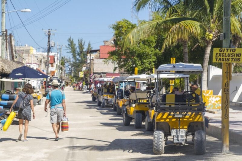 Person walking down street past beach buggies parked on the side of the road in Isla Holbox, part of any great Yucatan Itinerary