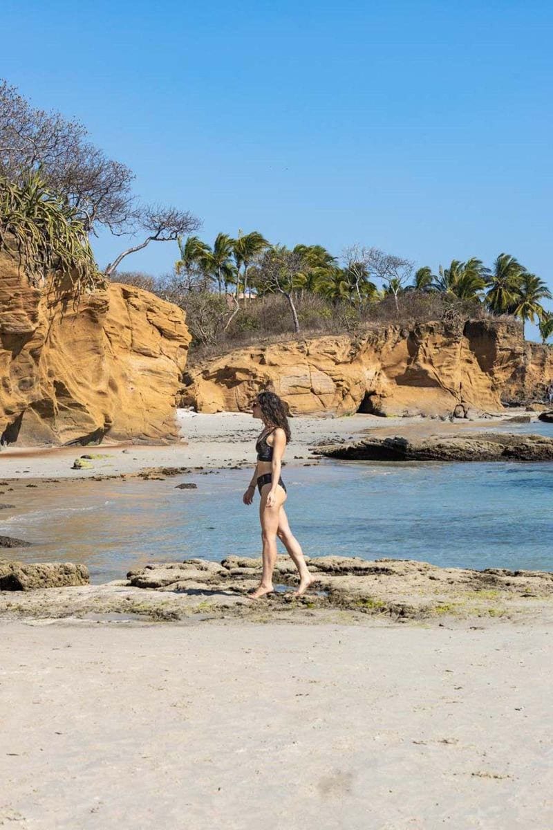 Woman walking on La Lancha Beach with rocky headland and ocean in background near Sayulita
