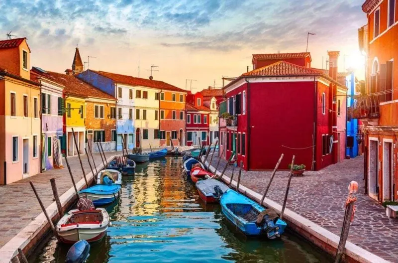 Sunset over canal with boats on each side and colorful buildings on Burano - one of the best day trips from Venice