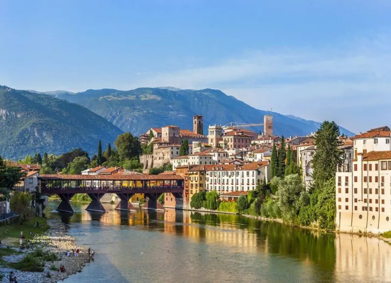 Old Bridge over river with historic buildings and mountains in background in Bassano - one of the best day trips from Venice 
