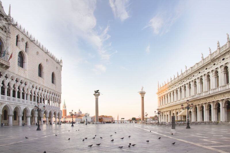 Piazza San Marco at sunset with pigeons on piazza and buildings each side of piazza - add San Marco Piazza to your Venice Itinerary