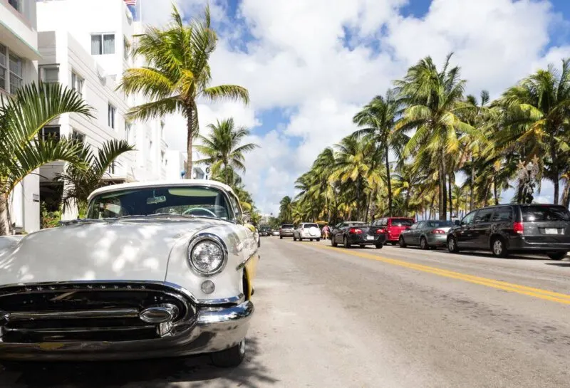 Classic car parked on side of road with palm trees and buildings lining the street in Miami