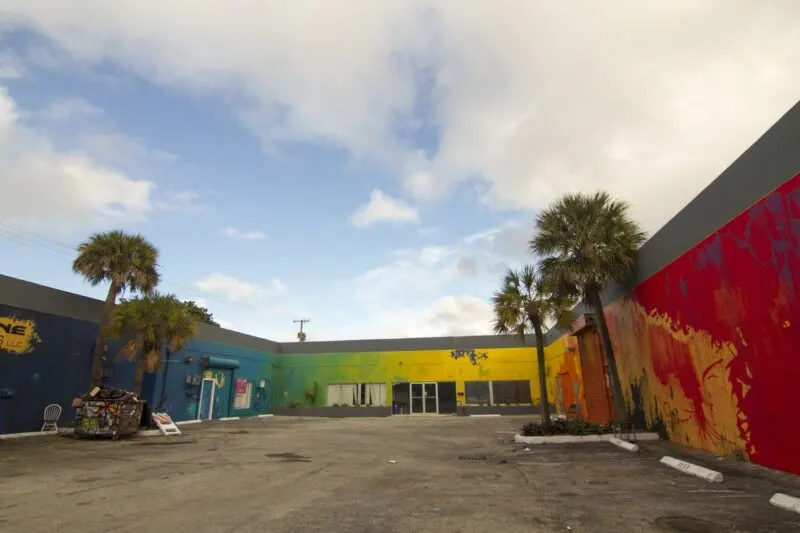 Colorfully painted walls in a U shape around concrete carpark and palm trees in Wynwood, Miami