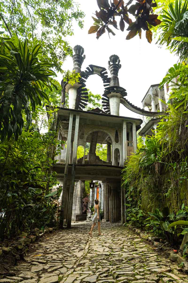 Nina along a path leading up to unusual gate surrounded by foliage in Las Pozas Xilitla Jardin.