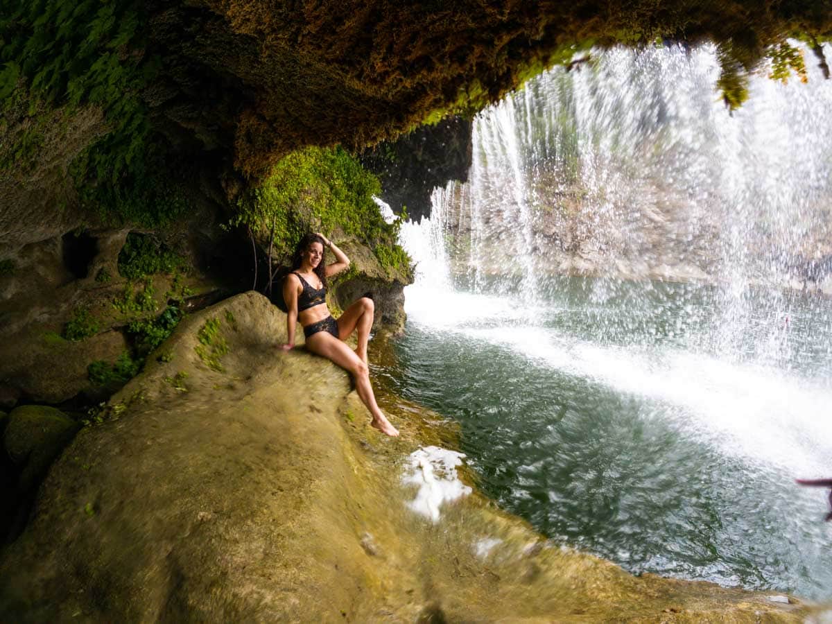 Nina in a black bathing suit posing on rock in cave behind Micos Waterfall.