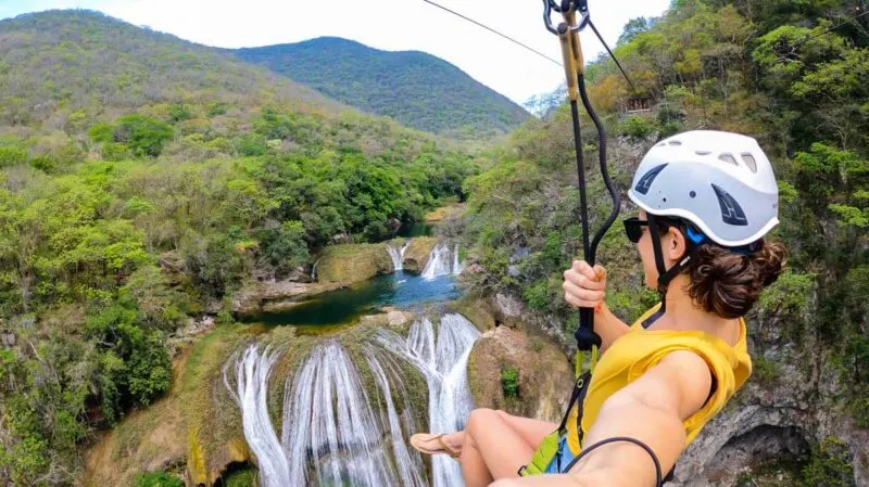 Nina ziplining over Micos Waterfall with jungled mountains in background on a Huasteca Potosina tour