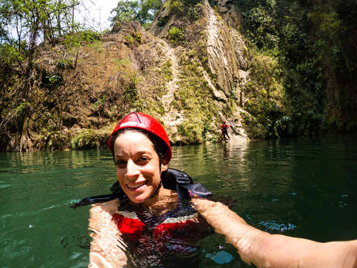 Nina taking a selfie in the water of Minas Viejas with helmet and lifejacket on with cliff in background.