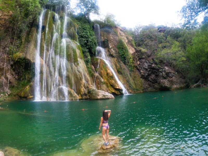 Nina standing on rock in waterfall pool looking at Minas Viejas waterfall. She planned the trip during shoulder season in Mexico