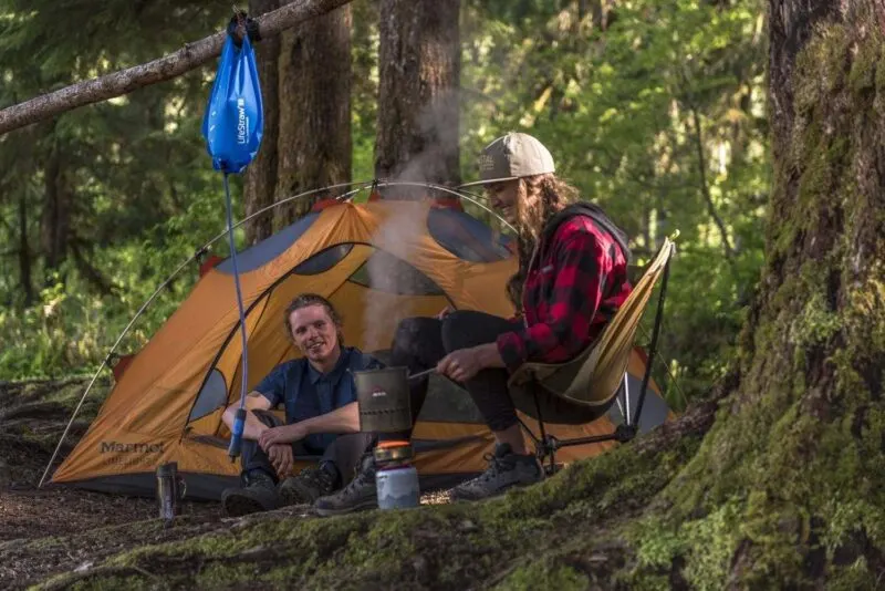 LifeStraw Flex Advanced Gravity Water Filter hanging at campsite with two people sitting around in front of orange tent - one of the best travel water filters