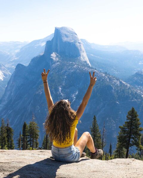 Woman sitting on cliff at Glacier Point on a Yosemite road trip