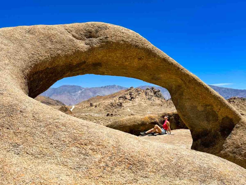 Woman sitting under Mobius Arch in the Alabama Hills, California on a California road trip