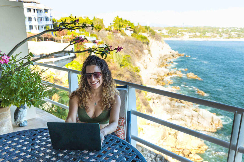 Nina working on laptop as a digital nomad with beach behind here, much happier