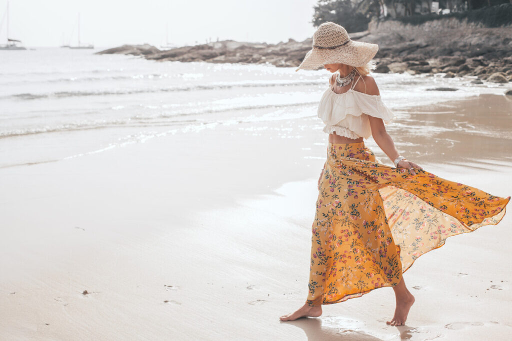 Woman wearing hat and flowy dress on beach for Thailand packing list