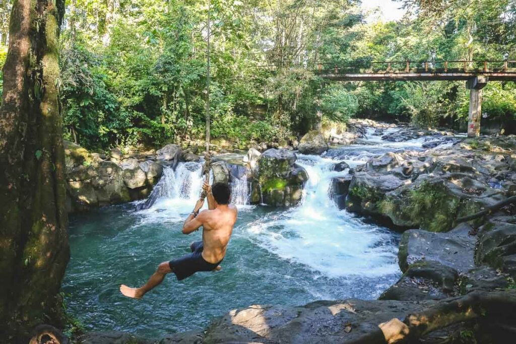 A man swinging from El Salto rope swing over the water-one of the best things to do in La Fortuna!
