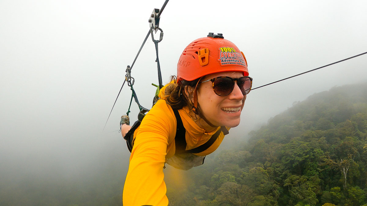 Nina ziplining in Monteverde in the foggy cloud forest wearing a red helmet, yellow jacket and sunglasses.