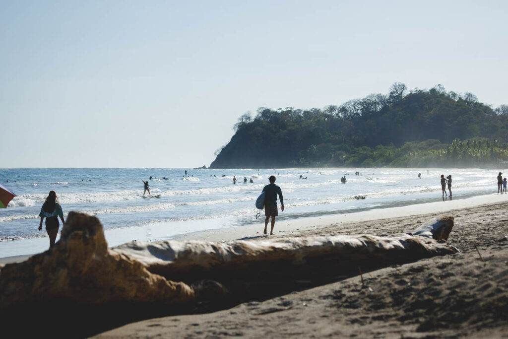 A surfer walking along Samara beach at golden hour.