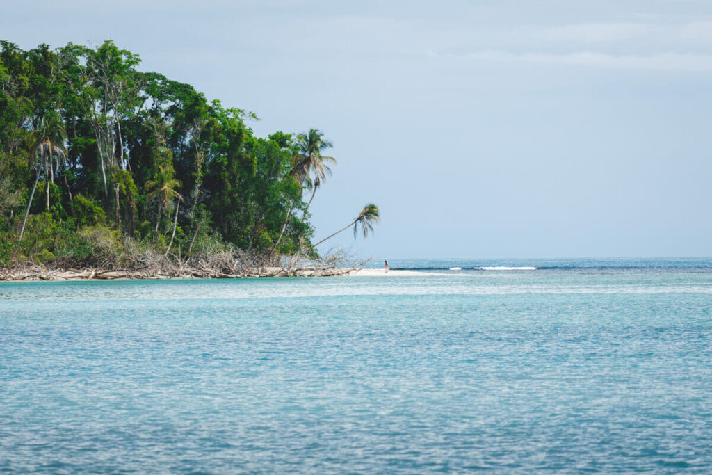 A lone tourist stands on a white sand beach surrounded by the blue waters of Cahuita National Park.