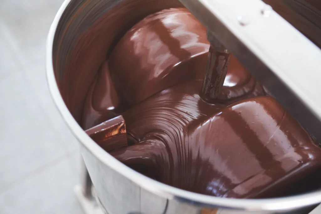 Melted chocolate being stirred in a stainless steel mixer.