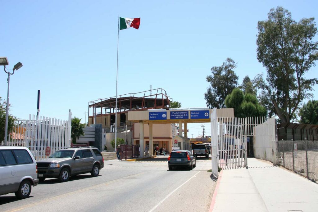 A Mexican flag flying over a Mexico-USA border crossing.