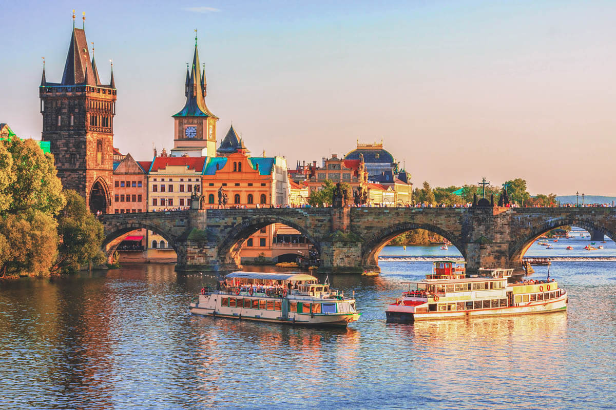 The sunset light glowing on Charle Bridge in Prague, Czech Republic, as tour boats cruise around on the Vltava River.