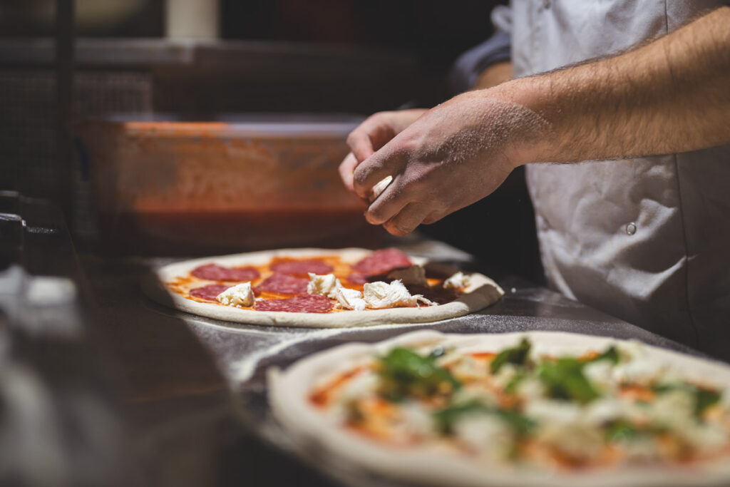 A male chef preparing the bases for stone baked Italian pizza for customers to try.