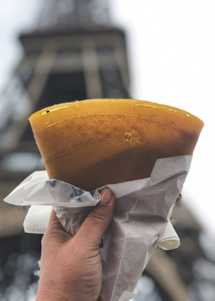 A female hand holding up a crepe in Paris right in front of the Eiffel Tower.