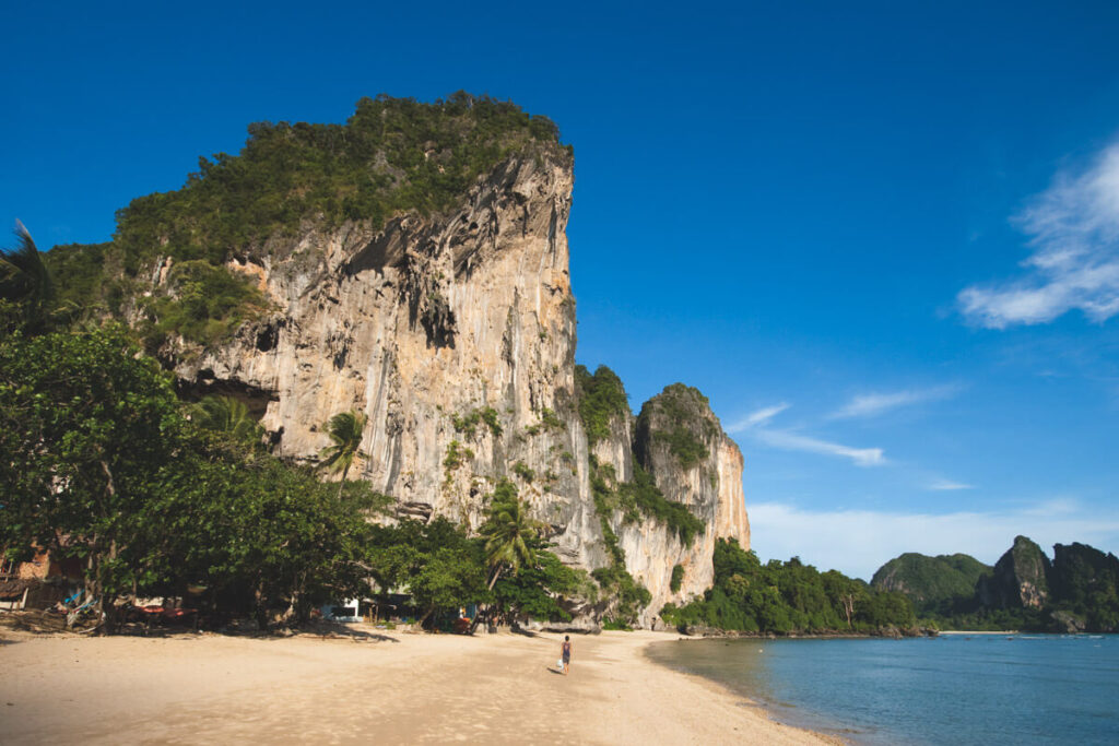 One tourist walking alone along Tonsai Beach in Krabi with a huge limestone cliff as a backdrop.