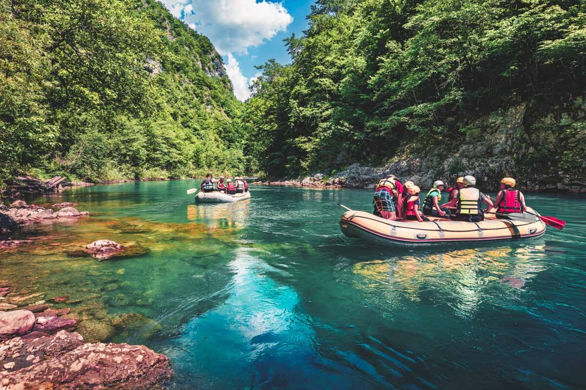Two groups of rafters drifting along the clear blue waters of the River Tara in Montenegro, surrounded by trees - a great experience in Europe.