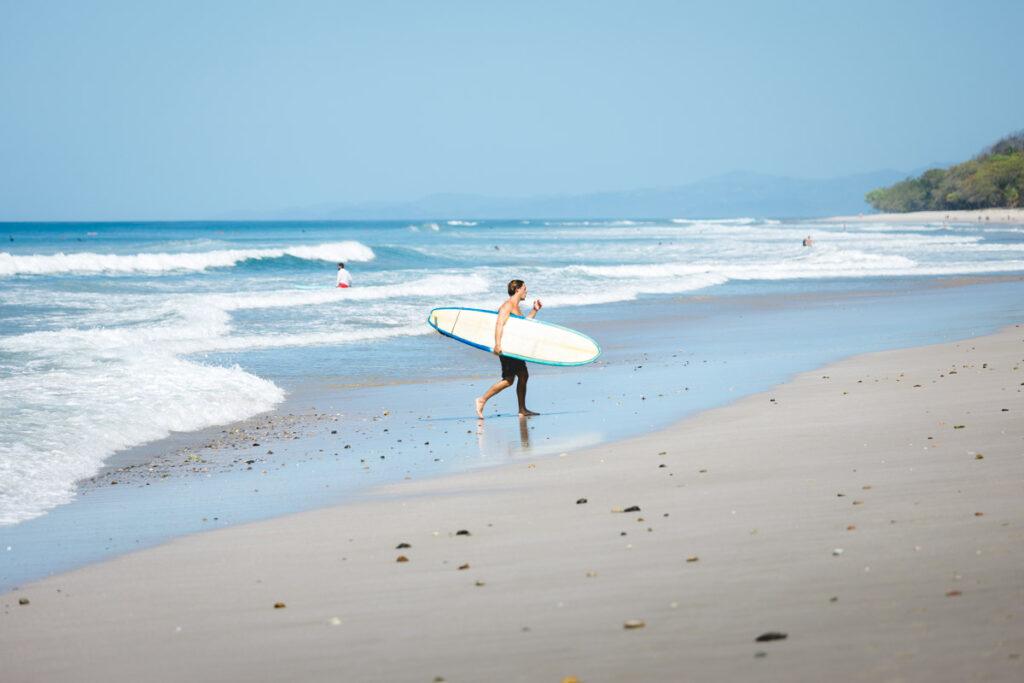 A man holding a surfboard walking along Santa Teresa Beach.