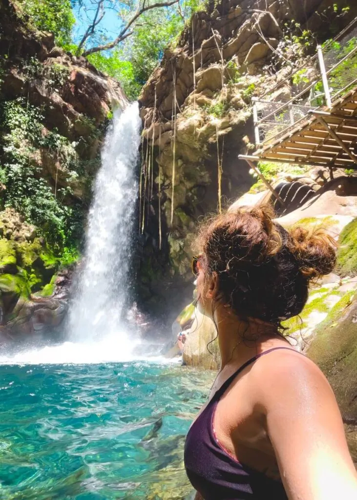 Woman paddling in Oropendola Waterfall plunge pool while watching the falls and taking a selfie.