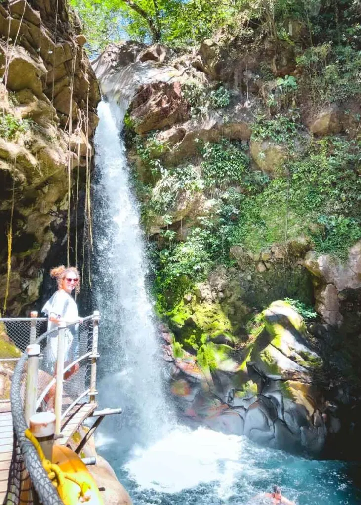 Woman standing on the waterfall viewing platform and smiling while people below are swimming.