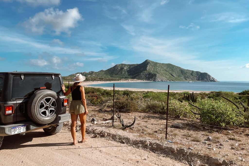 Female traveler standing besides a jeep looking out over Cabo Plumo.