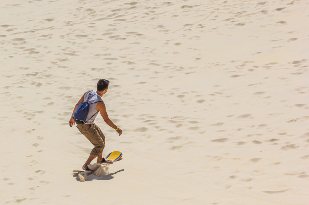 A man sand boarding down dunes in a desert.