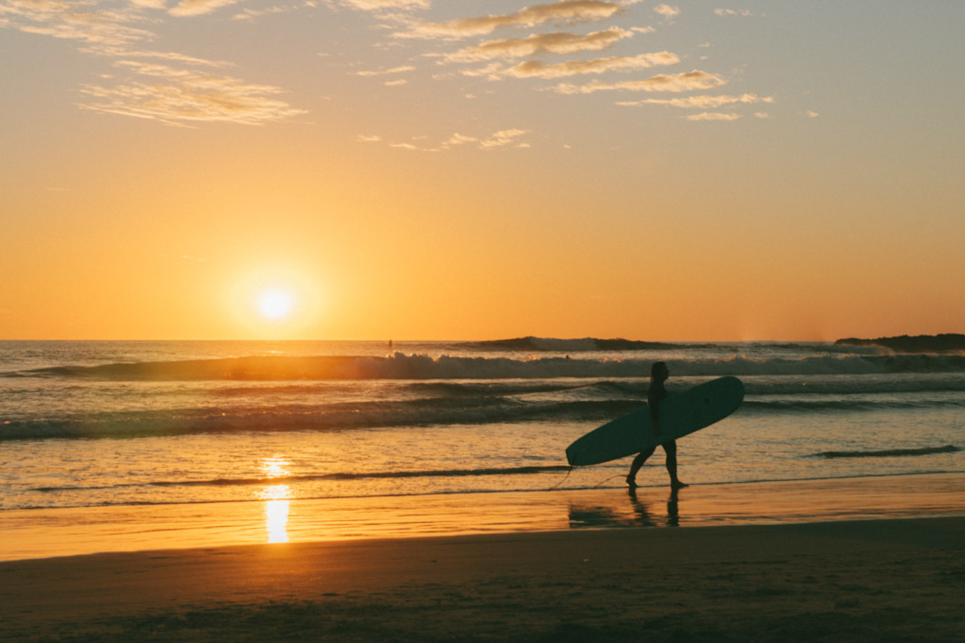 A surfer carrying a board along Cerritos Beach at sunset. A surfer carrying a board along Cerritos Beach at sunset.