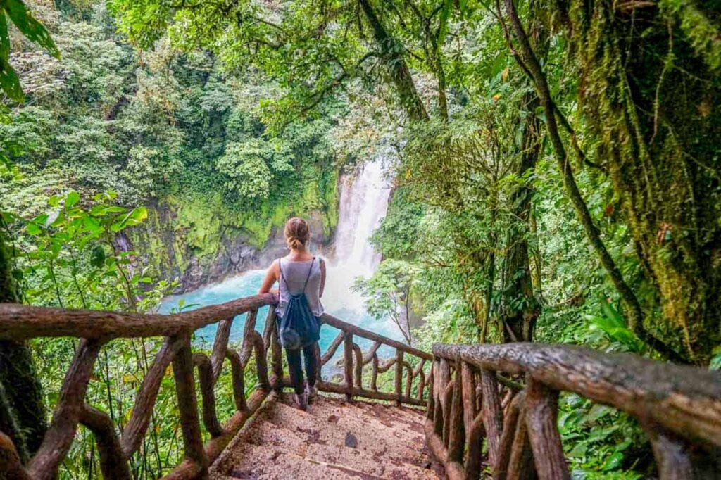 Woman standing on stairs looking down to Rio Celeste Waterfall.