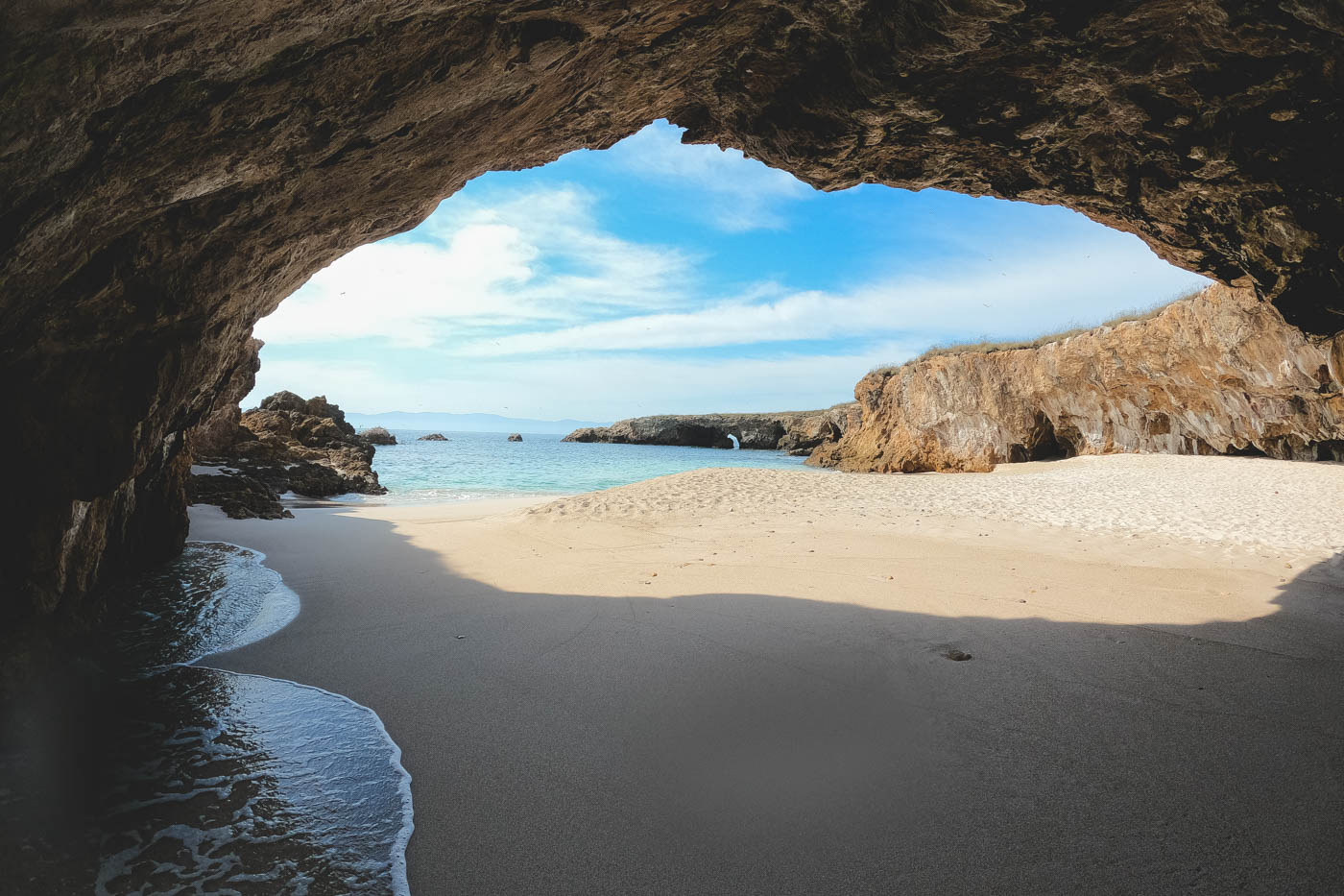 Arch way of rock with a beach leading to the ocean.