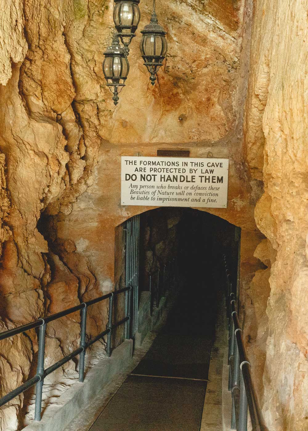Entrance stairway leading downwards though a tunnel with a sign above saying not to touch the formations in Crystal Caves.