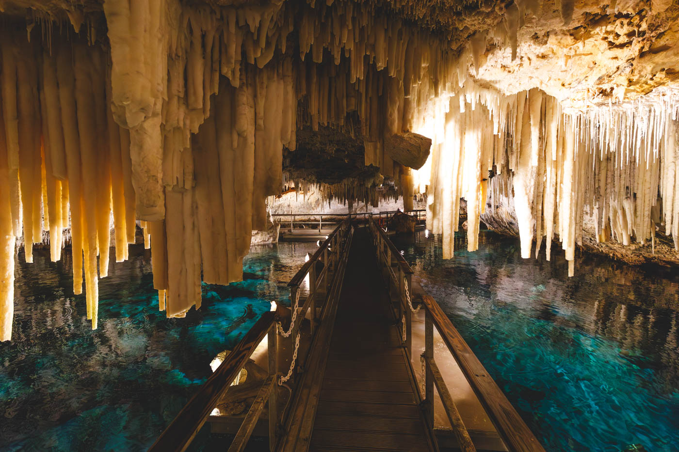 Walking on the Pontoon floating bridge with huge stalactites handing down on either side and crystal clear blue water below in Crystal Caves. 
