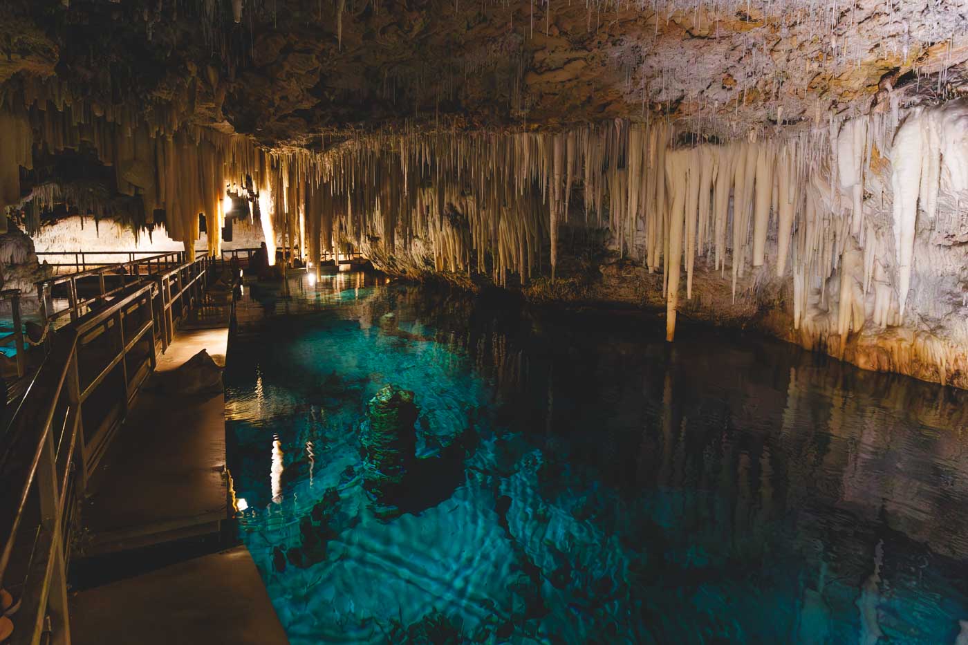 Looking to the right of the floating boardwalk to see the cavern ceiling full of stalactites along with stalagmites in the water below reaching upwards. 