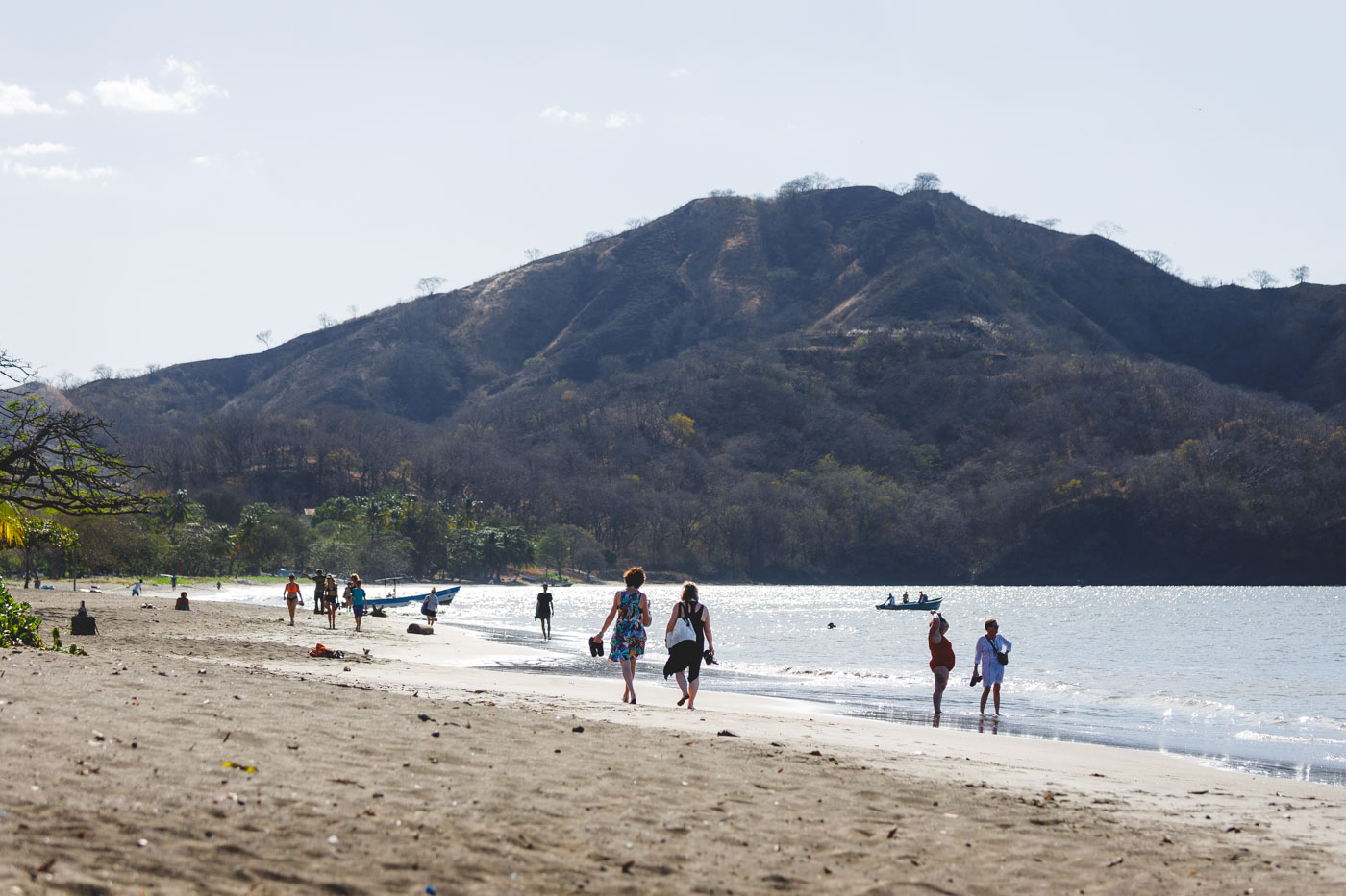 Tourists walking up and down Playa del Coco with a view of a mountain in the background.